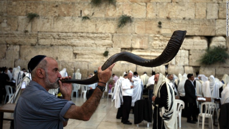 上图：一个犹太人于犹太新年在西墙吹响公羊角制成的羊角号（shofar）。犹太人被掳巴比伦回归以后，吹角节成为犹太人的农历新年（Rosh Hashanah），这一天要一百次吹响羊角号。